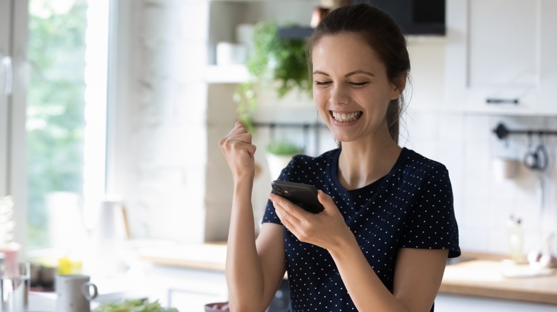 Woman laughing at cell phone in kitchen