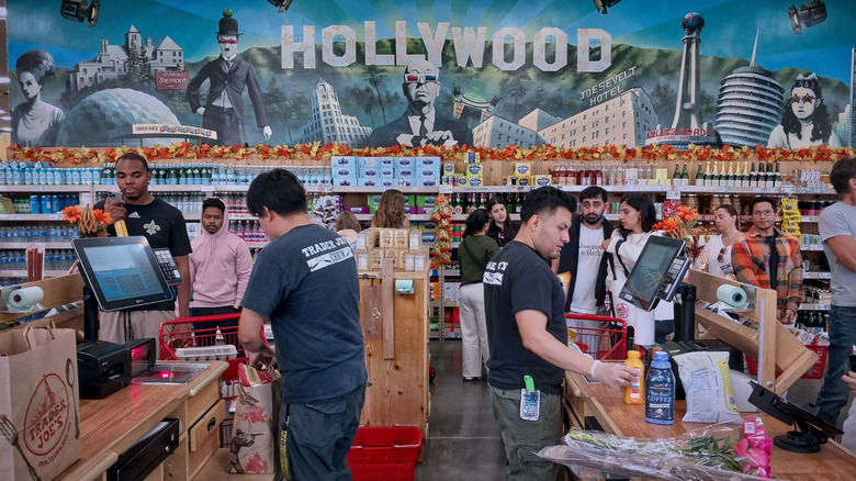 Trader Joe's employees assisting customers at checkout under a painter mural
