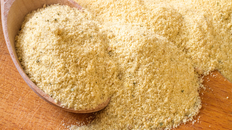 A wooden spoon scooping up chicken stock powder of a wooden surface