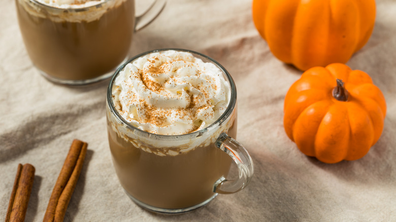 Pumpkin lattes surrounded by mini pumpkins and cinnamon sticks