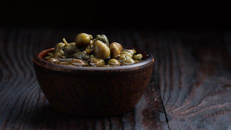 capers and brine in clay cup on dark setting
