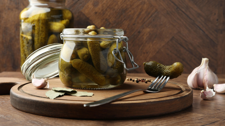 open pickle jar, fork, garlic, and herbs on wooden cutting board