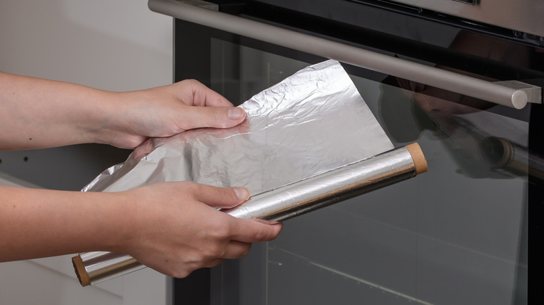 Person holding aluminum foil near oven