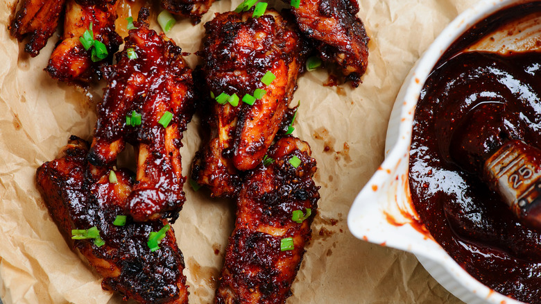 Applying BBQ sauce with a large brush to a hot, smoking grill full of assorted meats