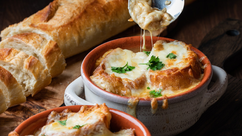 Two bowls of French onion soup topped with bread and cheese with a sliced baguette on the side