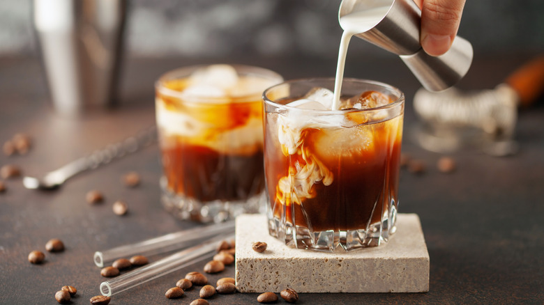 two tumbler glasses with coffee liqueur and cream being poured in