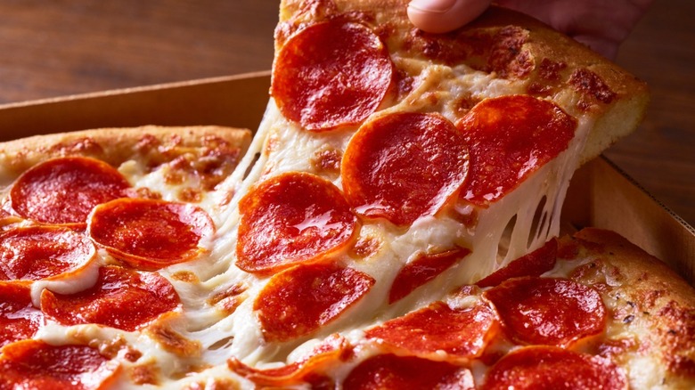 Closeup of a hand grabbing a fresh slice of pepperoni pizza