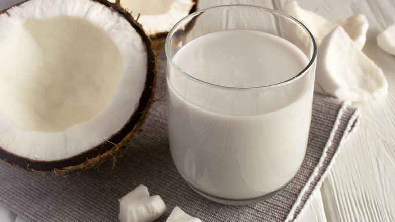 Glass of coconut milk beside open coconut 