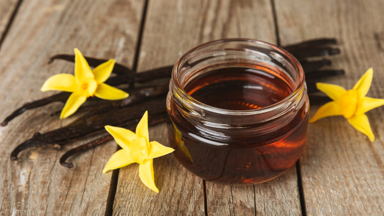 a small glass container of pure vanilla extract beside vanilla beans on a wooden surface