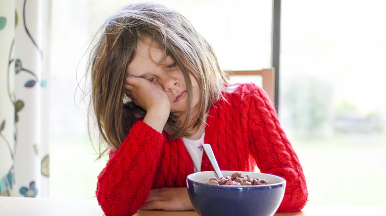 Girl sleeping behind cereal bowl 