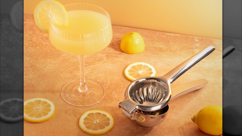 The Zulay Kitchen stainless steel hand juicer press on a counter with a cocktail and lemon
