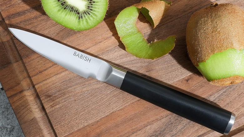 Close-up of the Babish paring knife on a cutting board with cut and partially peeled kiwi