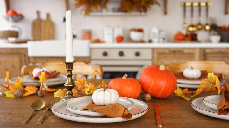 A kitchen with a fall table setting of pumpkins, golden leaves, and candles