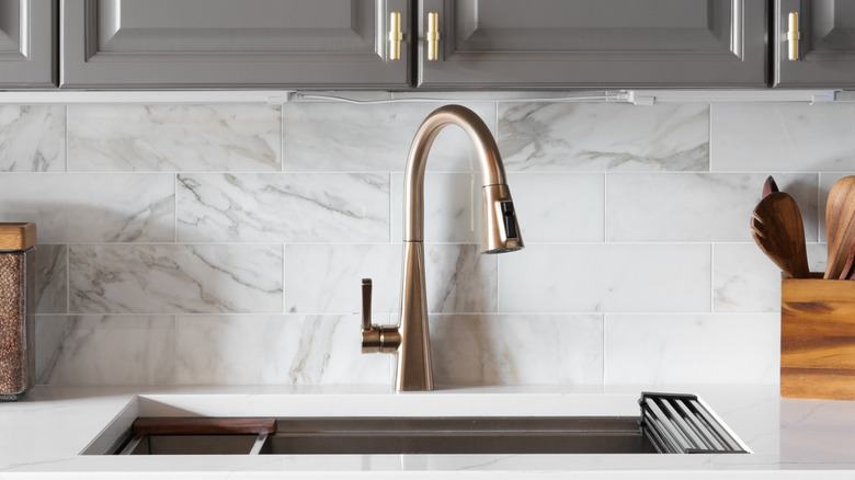 Broze-colored, high-arc, pull-down faucet in a marble-tiled kitchen