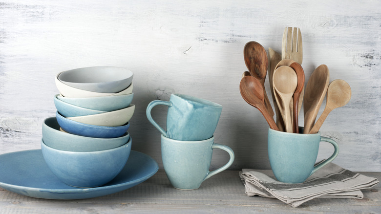 Stacks of blue dinnerware next to a mug full of wooden cooking utensils