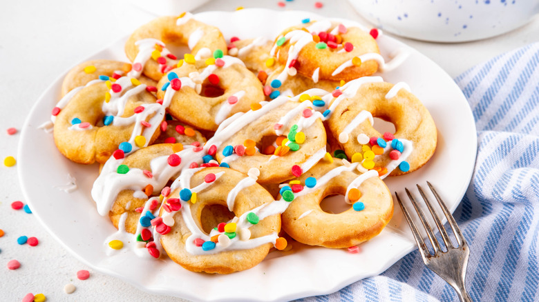 Donuts made with pancake mix on a white plate covered with white frosting and colorful sprinkles