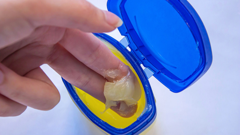 Person scooping petroleum jelly from container