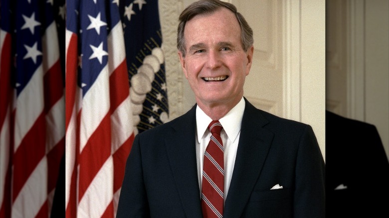 president george herbert walker bush smiling and standing next to the American flag