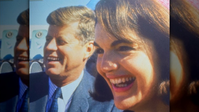 President John F Kennedy smiling in a sideways portrait with his wife Jackie in the foreground