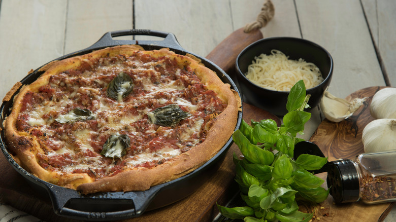 Pizza in a cast-iron skillet with shredded cheese, herbs, and garlic.