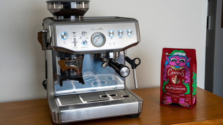 A Breville espresso machine is on a table next to a bag of coffee.