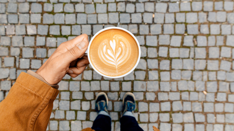 A person holds a coffee cup above a brick street