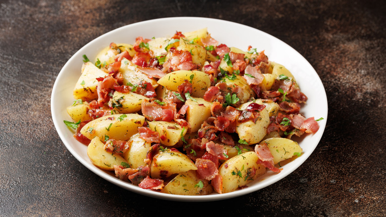 German potato salad with bacon and herbs on a white plate