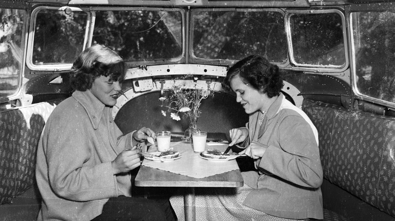 Two women seated at a table inside a plane enjoying a meal