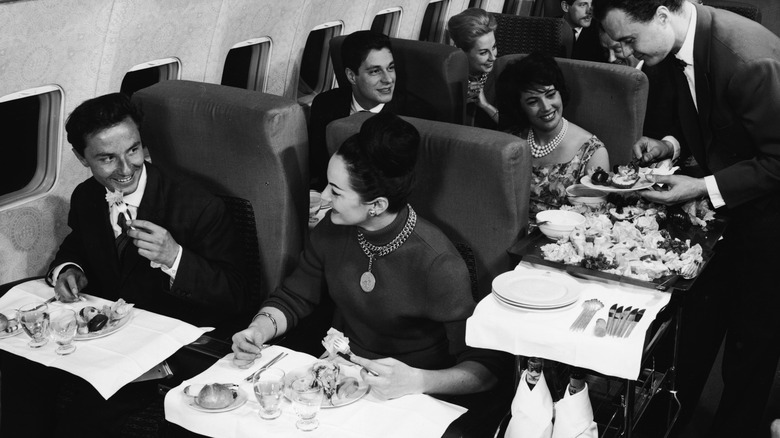 A couple smiles and enjoys their meal service onboard a plane in the 50s
