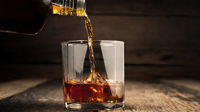 Pouring alcohol into glass; wooden background