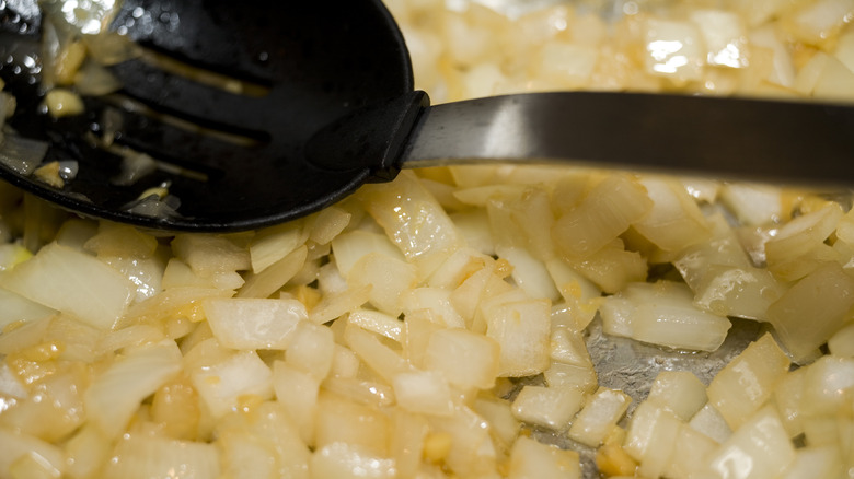 white onions sweating in pan with rubber spoon