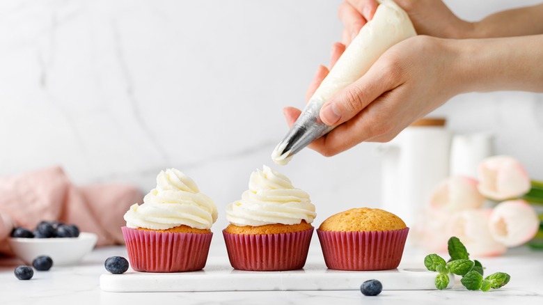 Three cupcakes being frosted with a piping bag
