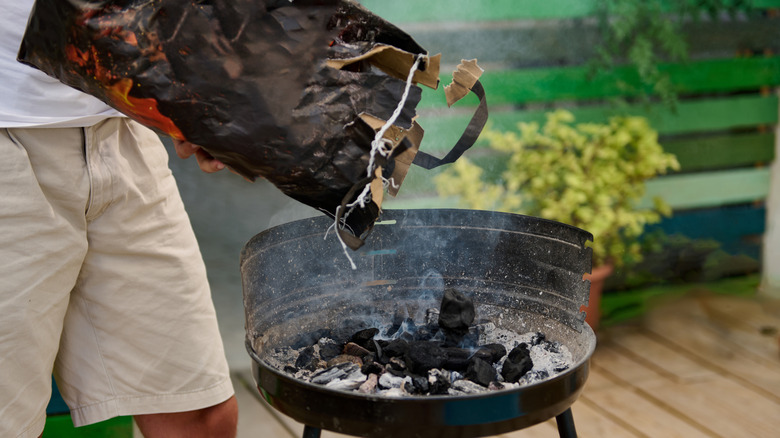 Person adding charcoal to grill
