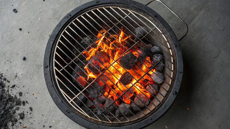 Charcoal burning in a charcoal grill with flames rising from the center