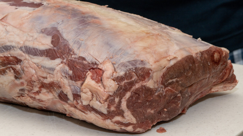 A large, raw, boneless prime rib with a slightly greyish-brown color