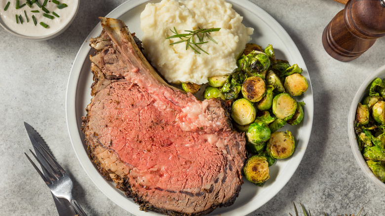 A prime rib slice with mashed potatoes and Brussel's sprouts on a dinner plate