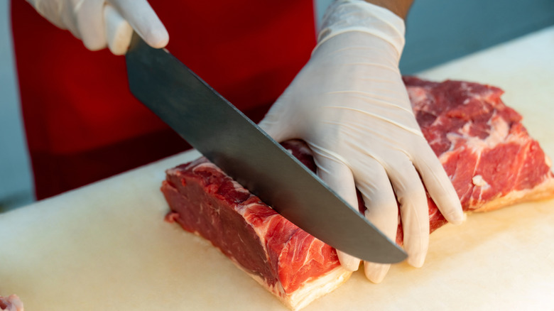 A close-up of a person wearing white gloves while slicing into raw beef