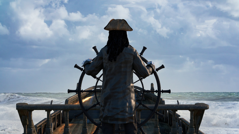 The back of a person dressed as pirate steering a small ship on the ocean