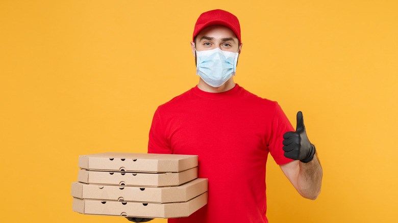 A delivery man wearing a face mask does a thumbs-up while holding pizza boxes