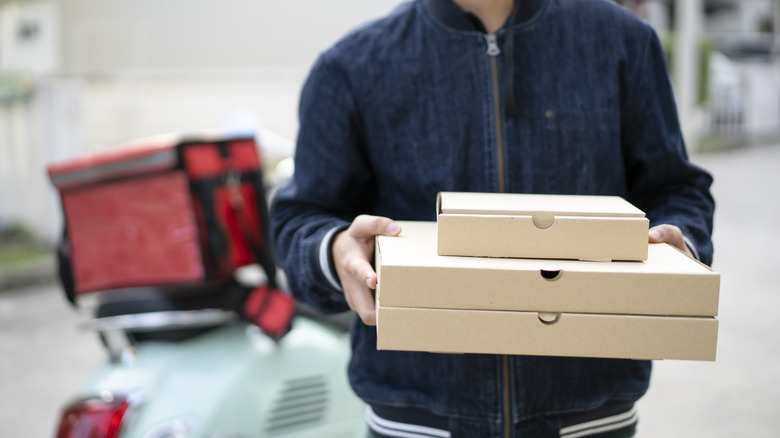 A pizza delivery man holds three pizza boxes, with a blurred motorcycle in the background