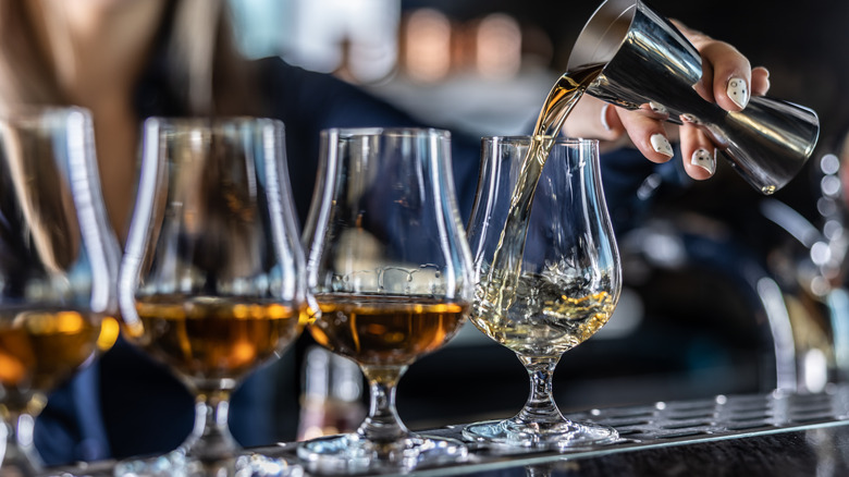 Bartender pouring bourbon into tulip-shaped glasses