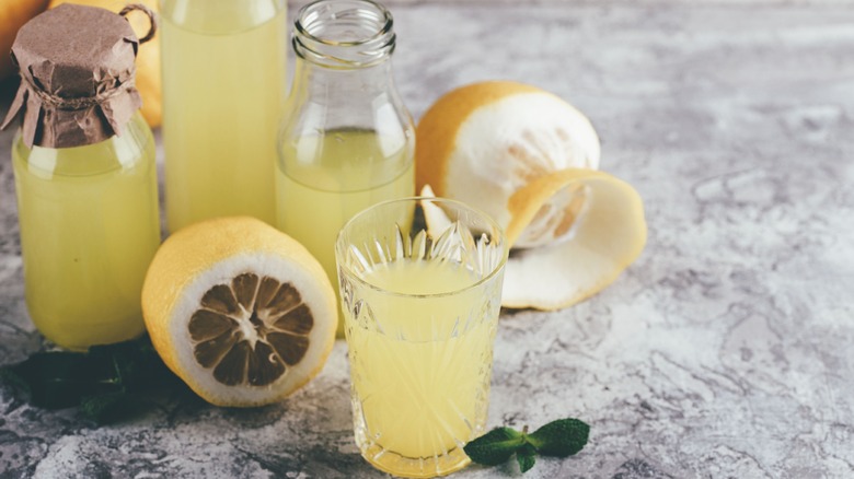 Bottles of homemade limoncello with a glass of it and a peeled lemon in front of them