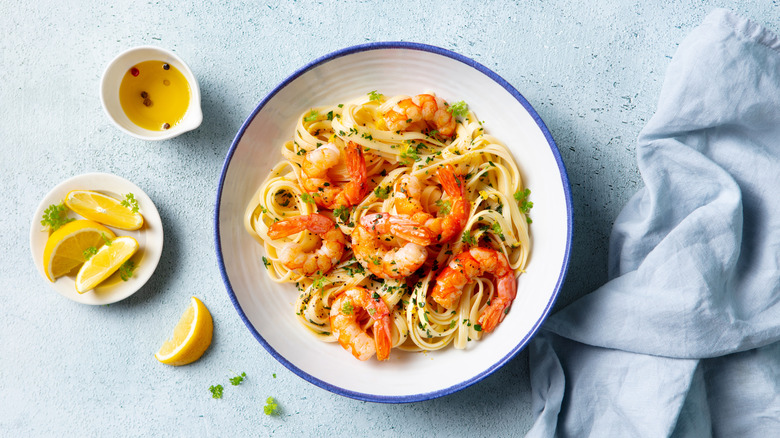 Shrimp scampi in a blue-rimmed white bowl with lemon wedges and olive oil on the side