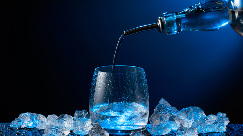 A glass of vodka, surrounded by ice, is poured from a bottle