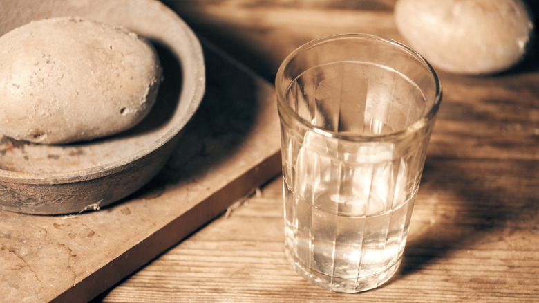 A glass of vodka or water sits next to potatoes