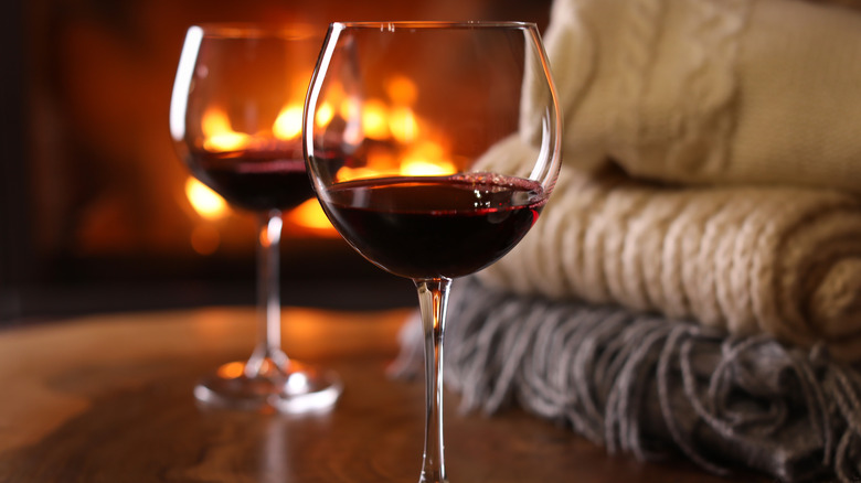 Glasses of red wine next to blankets in front of a fireplace