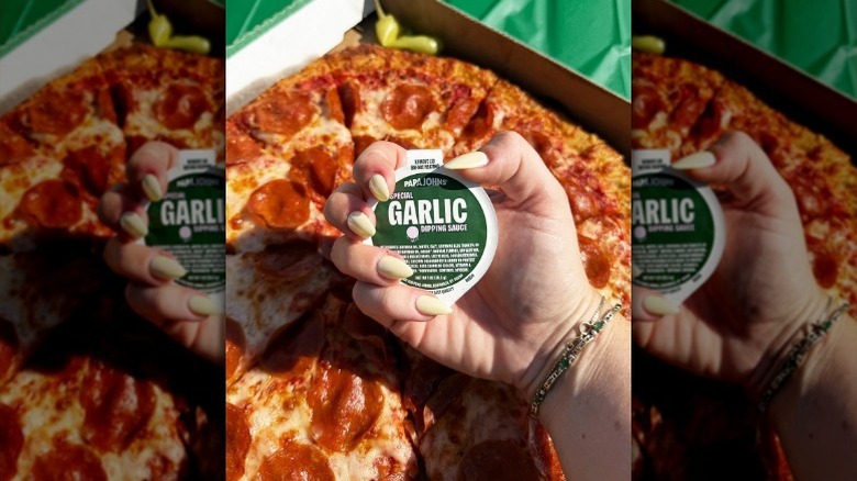 Hand holding garlic dipping sauce over pizza