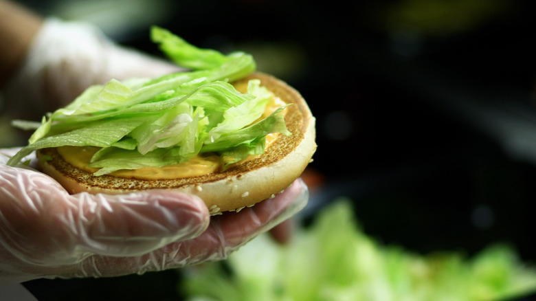 Employee holding a burger bun topped with lettuce