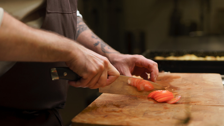 Chef cutting tomatoes on wooden cutting board
