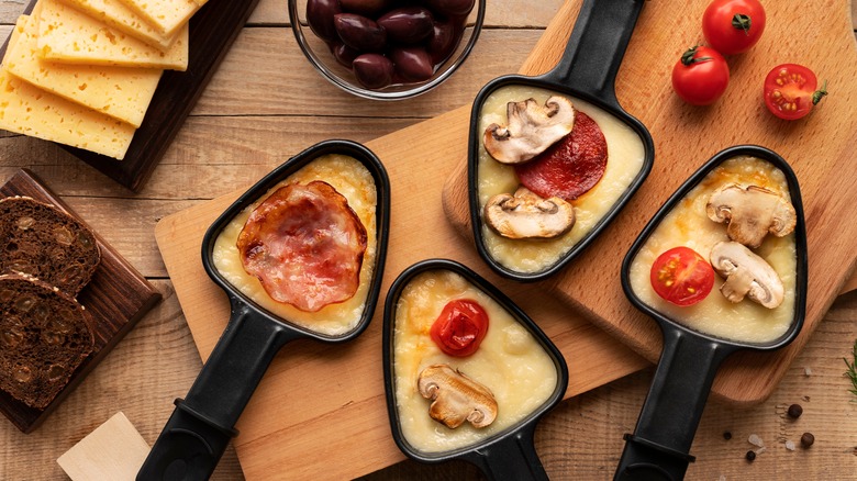 raclette in small skillets with toppings on wooden boards